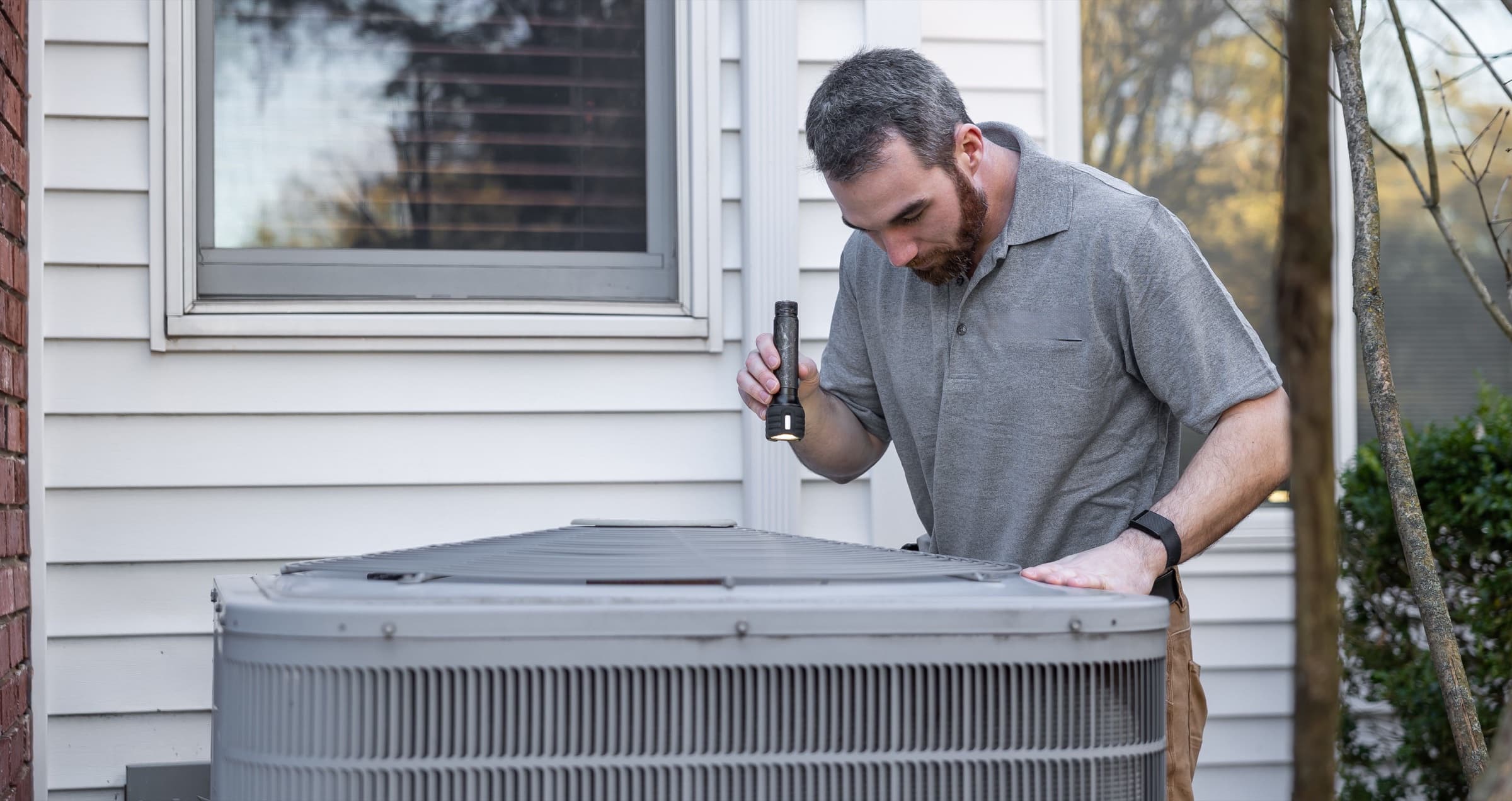 Residential HVAC technician inspecting an outdoor air-conditioning condenser